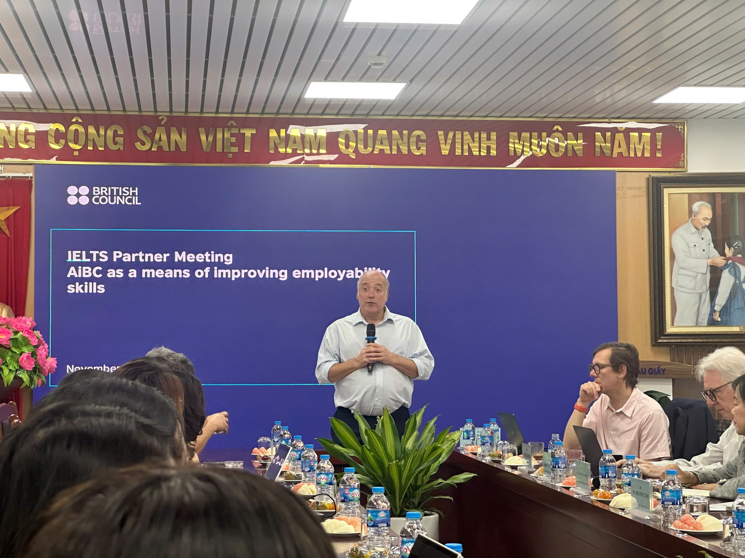 A person standing in front of a table with people sitting around it

Description automatically generated