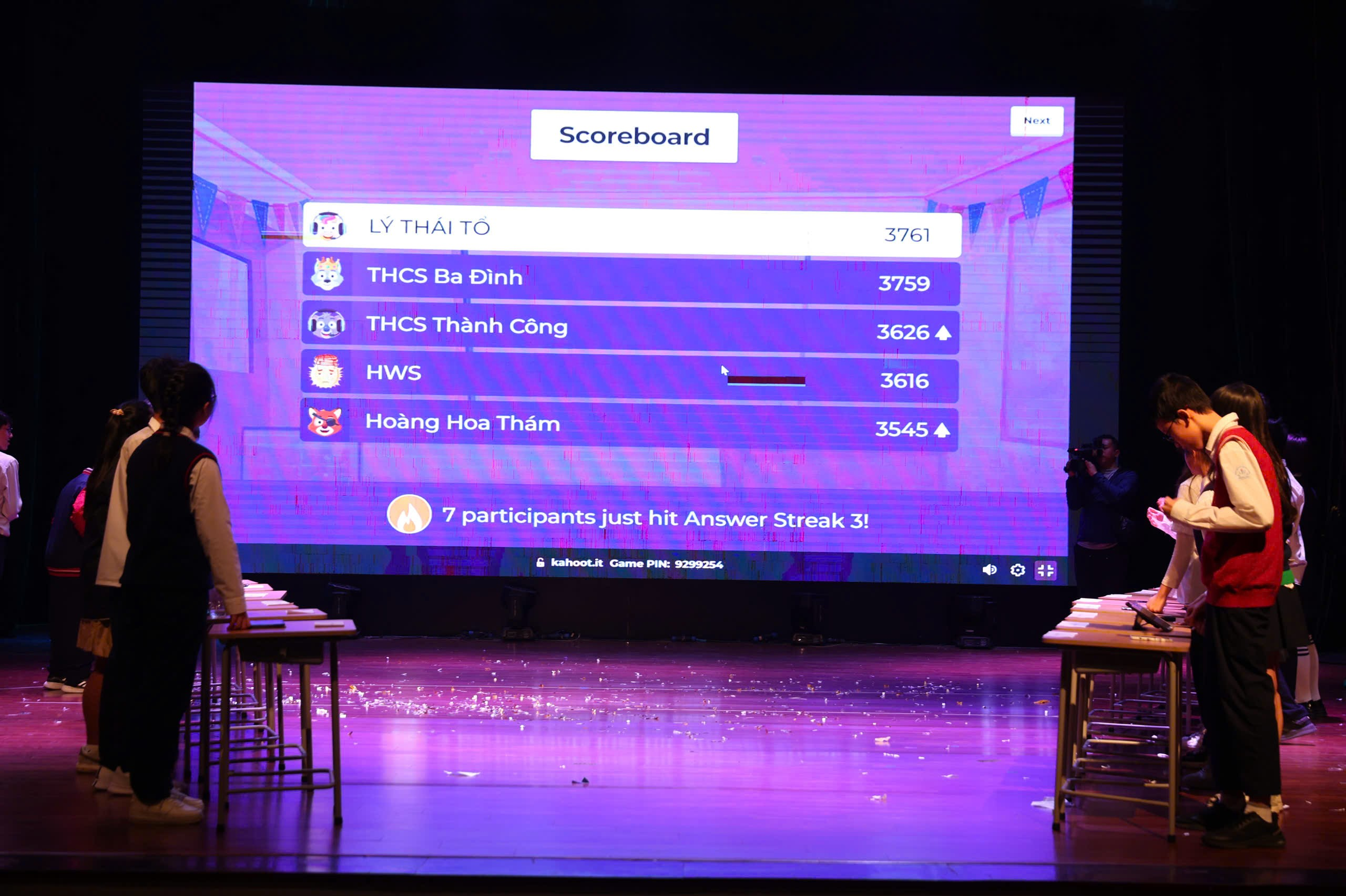 A person standing on a stage with a large screen
Description automatically generated