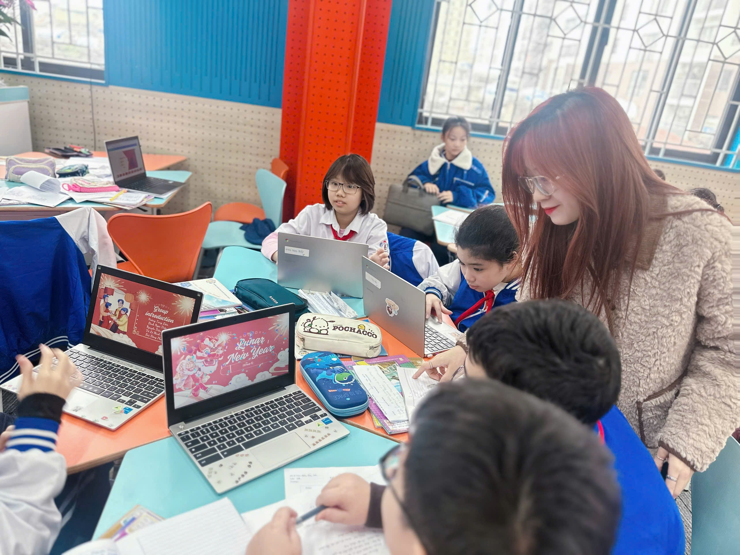 A group of children and a person in a classroom with laptops

Description automatically generated