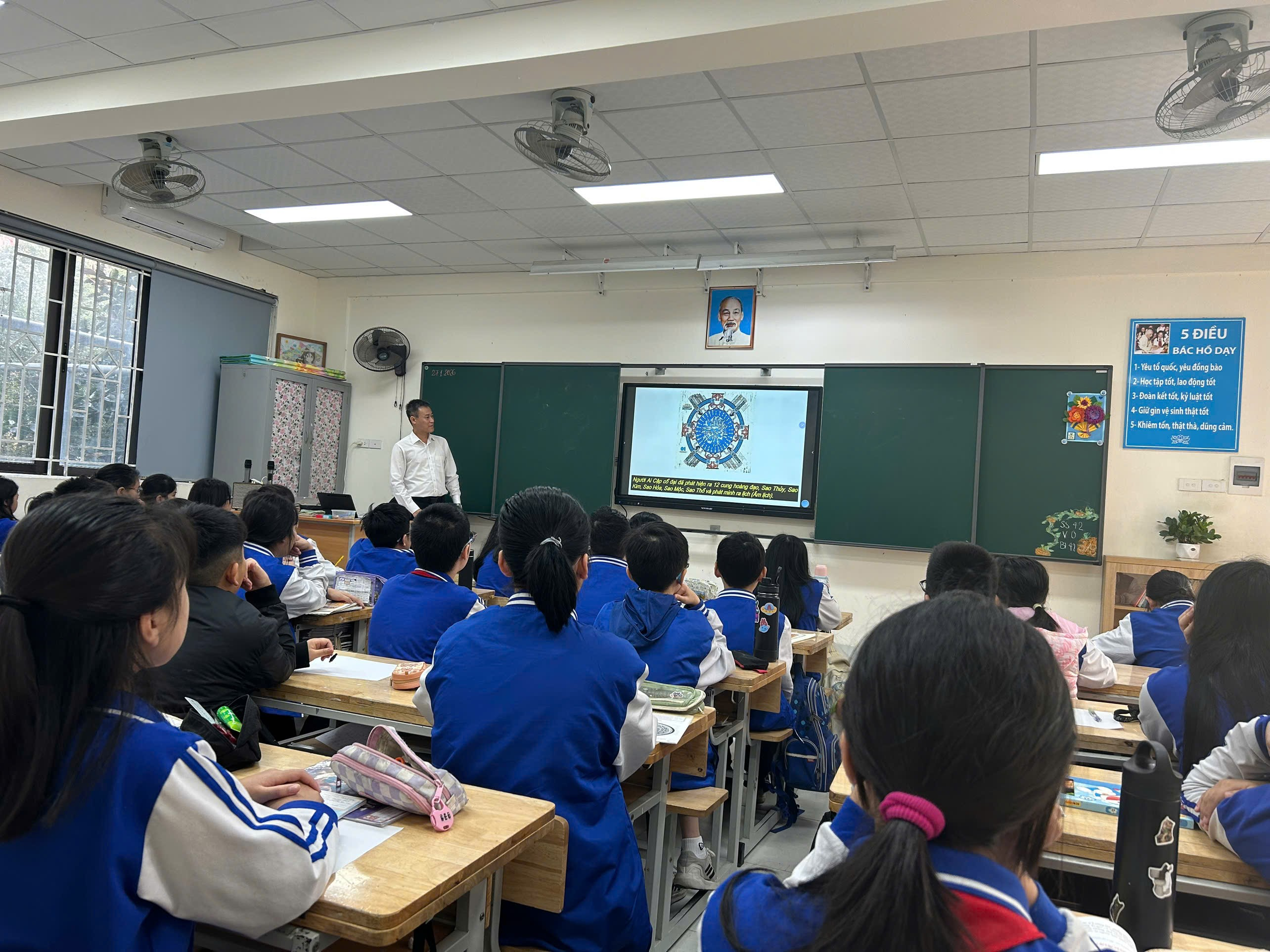 A classroom with a person in front of a classroom

Description automatically generated